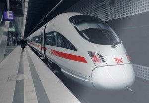Zug der Deutschen Bahn steht am Gleis. Eine Person in dunklem Mantel spaziert am Gleis entlang